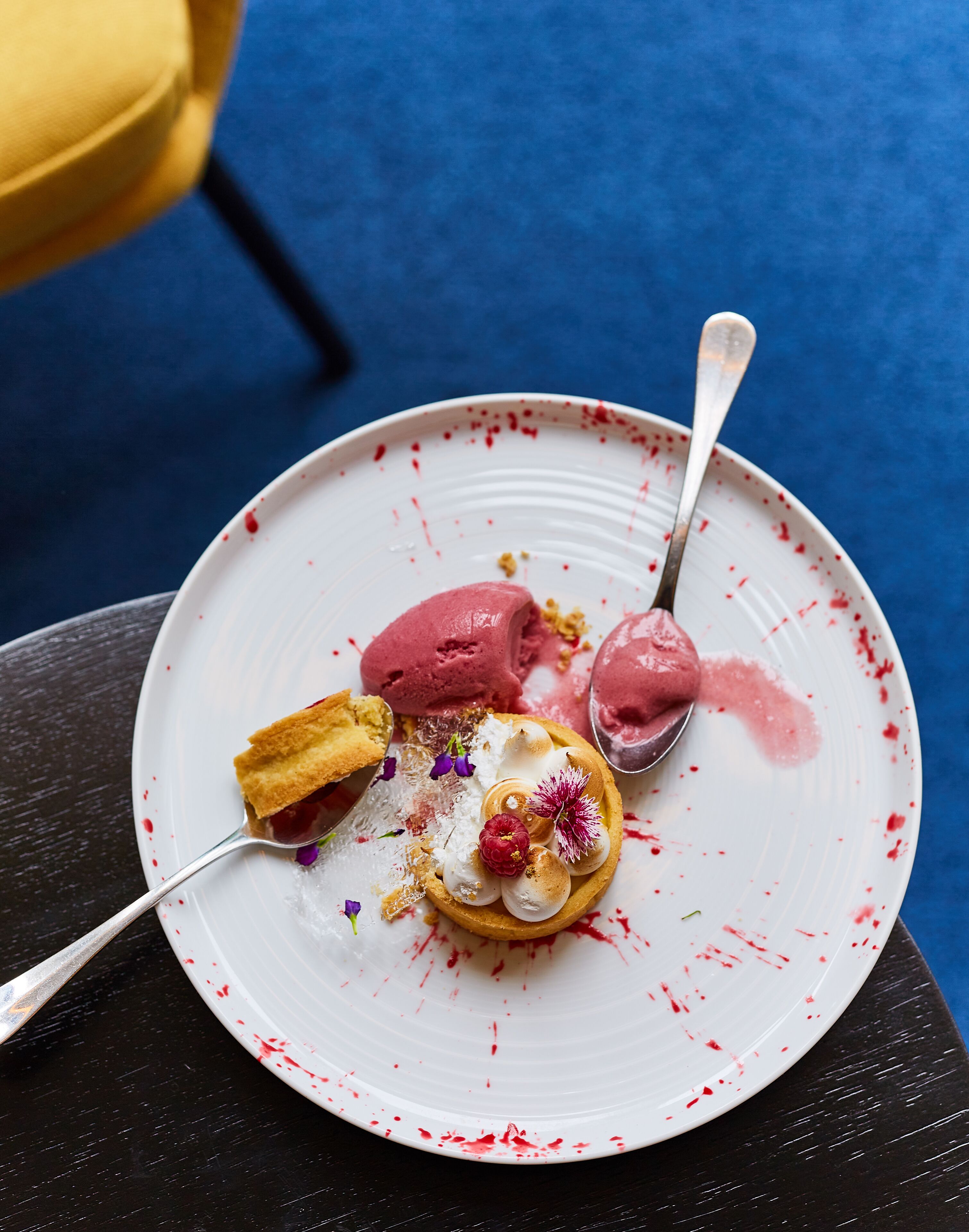 A dessert plate with a pastry, ice cream, and a spoon on a white plate with red splatters.