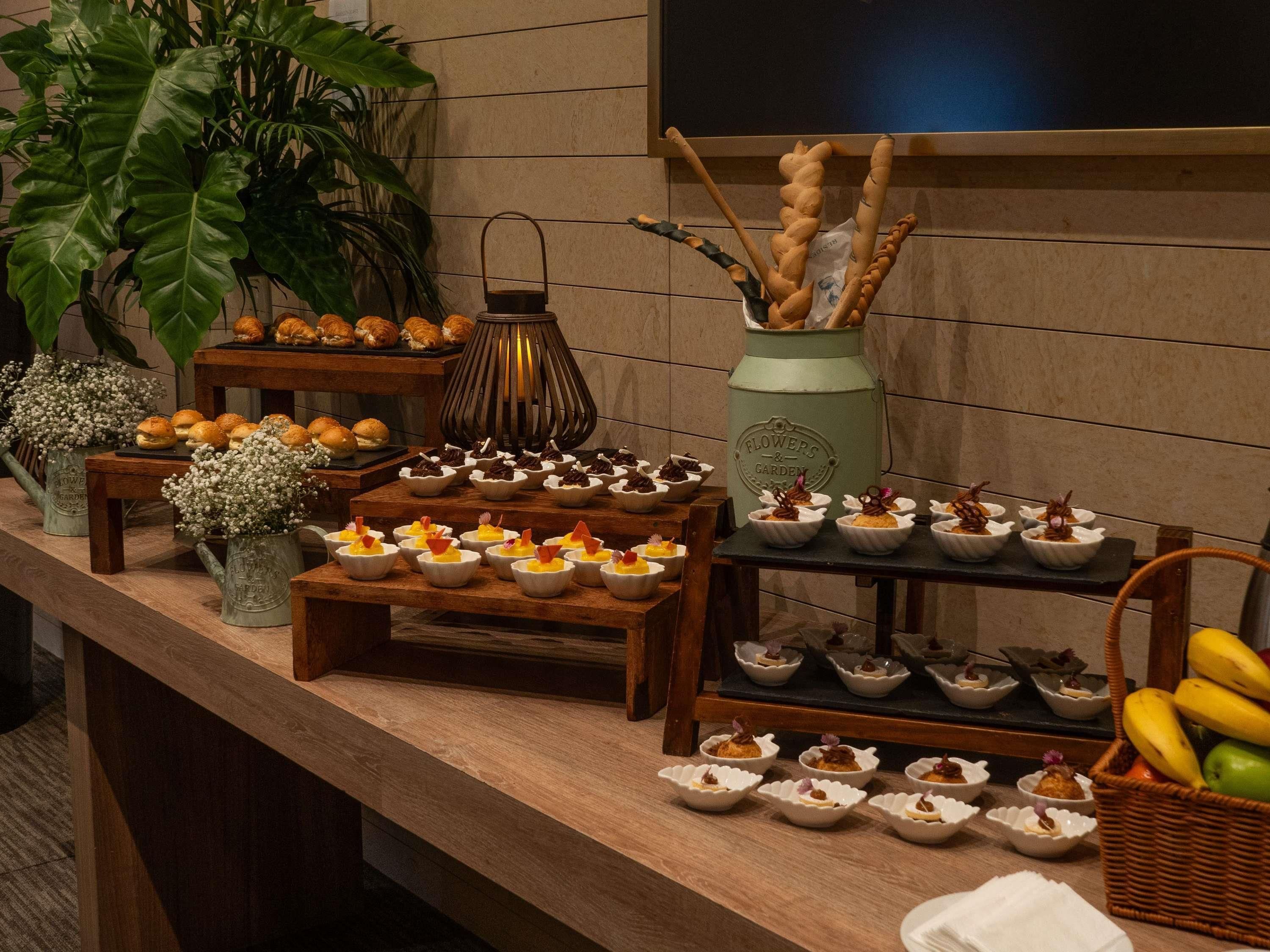 A buffet table with various food items, a vase with branches, and a television mounted on the wall.