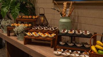 Una mesa de buffet con diferentes alimentos, un florero con ramas y un televisor montado en la pared.