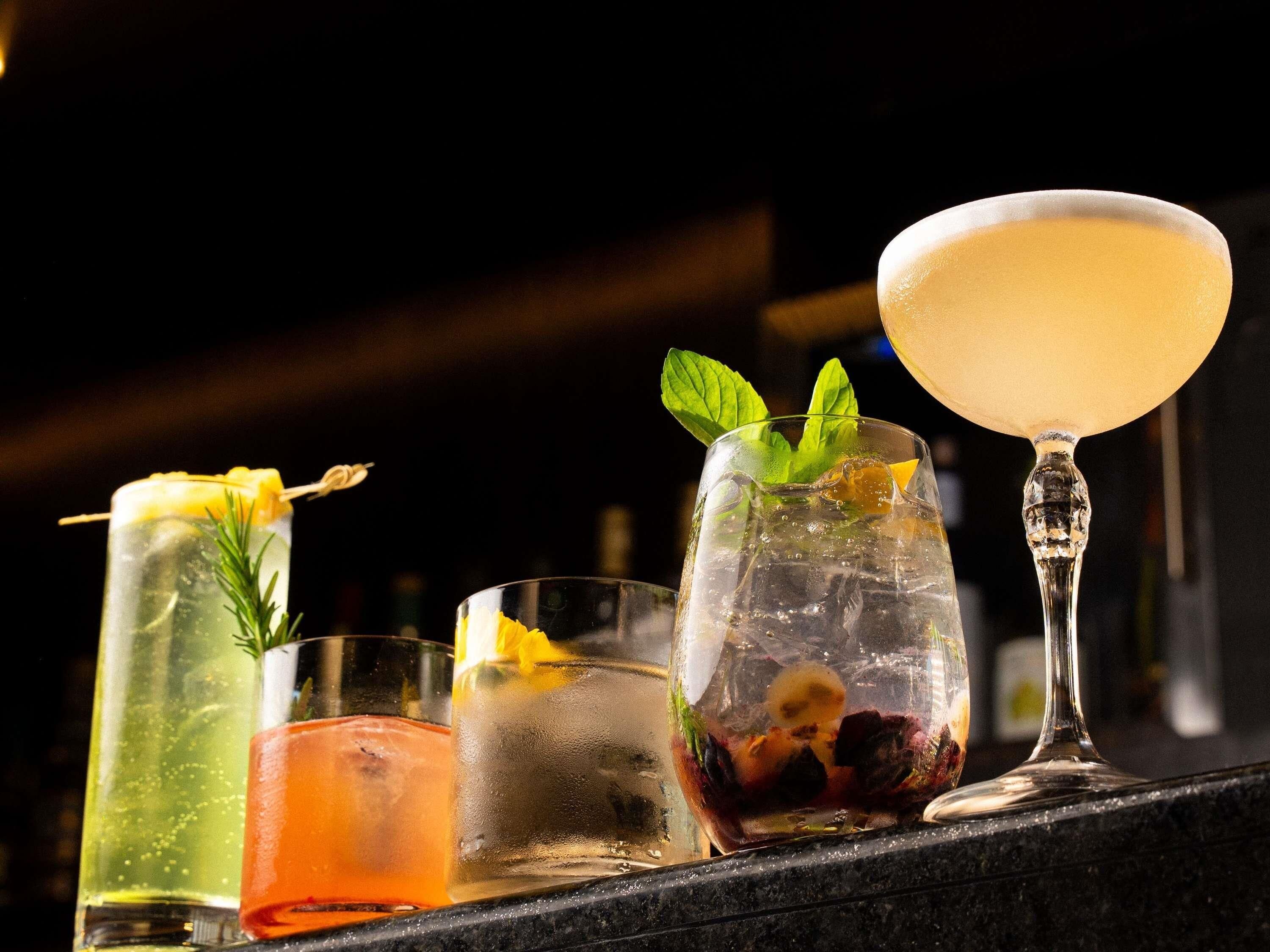 Un bar con diversas bebidas, incluyendo un martini, un cóctel con una rodaja de limón y un vaso con hielo y una ramita de menta.