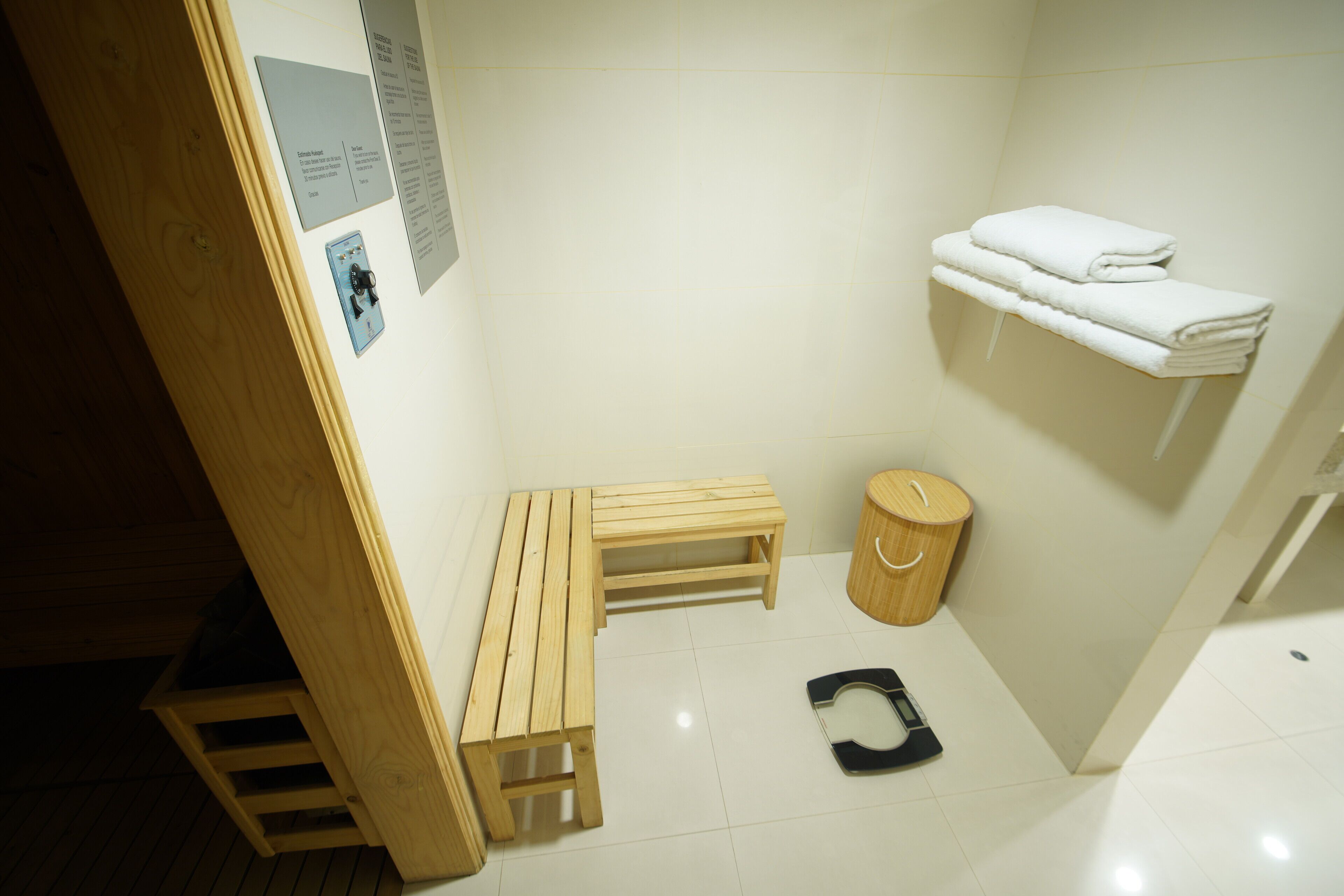 A small, clean bathroom with a wooden bench, a toilet, a shelf with towels, and a wooden trash bin.