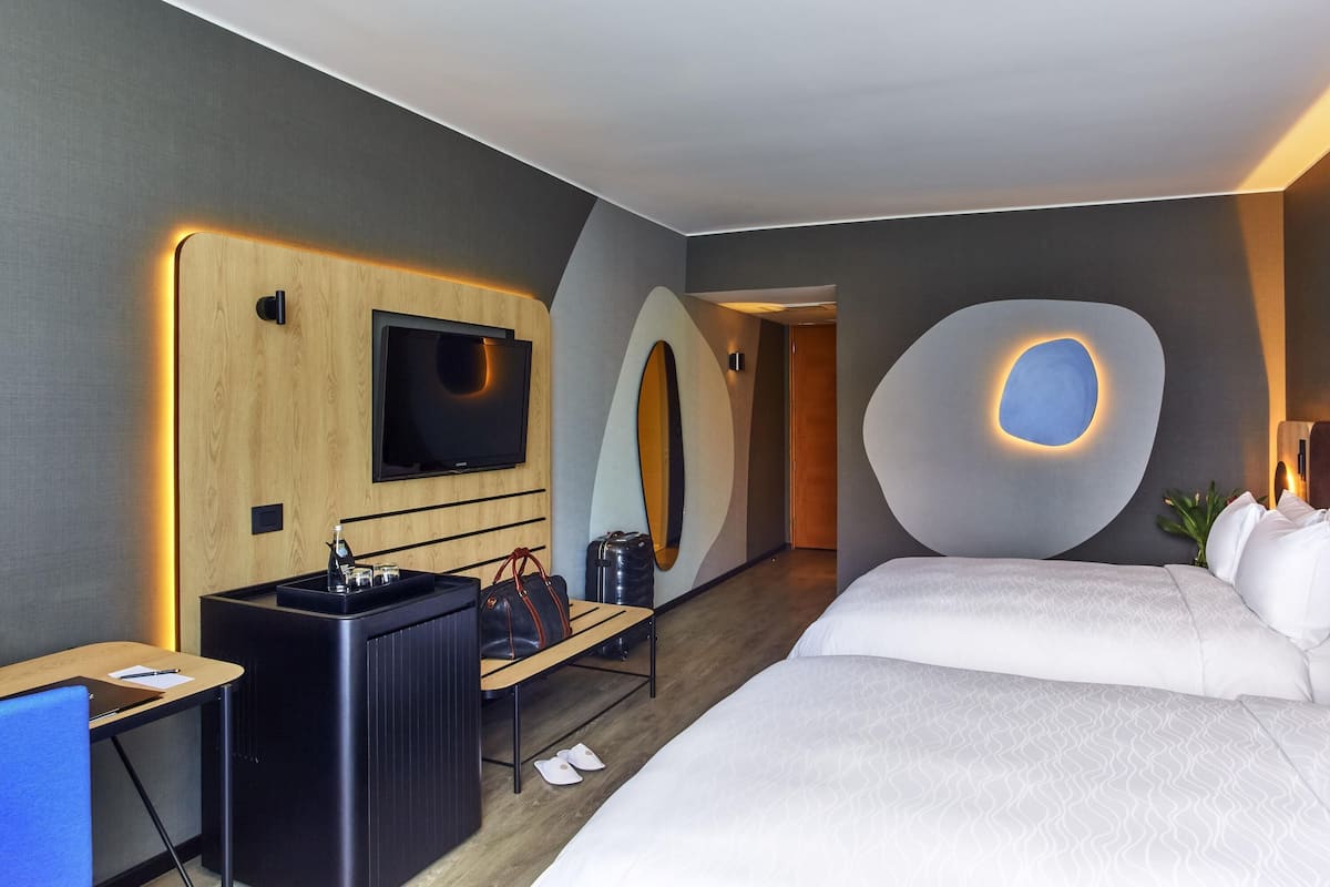 Une chambre dâhĂŽtel moderne Ă©quipĂ©e dâun lit, dâun bureau, dâune tĂ©lĂ©vision et prĂ©sentant un dĂ©cor mural original.
