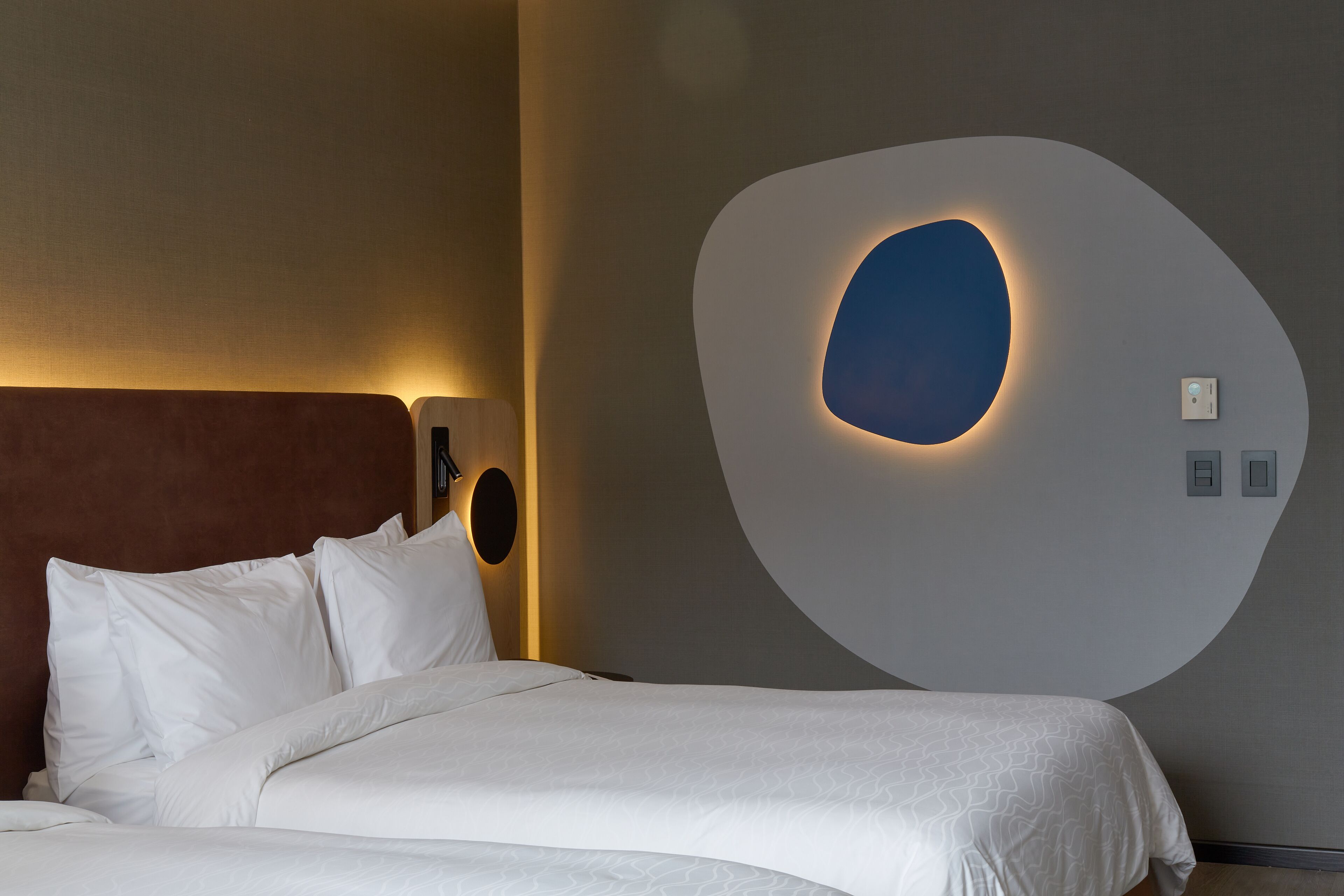 Une chambre d’hôtel moderne dotée d’un grand lit, d’un luminaire mural original et d’un élément décoratif mural rond et illuminé.