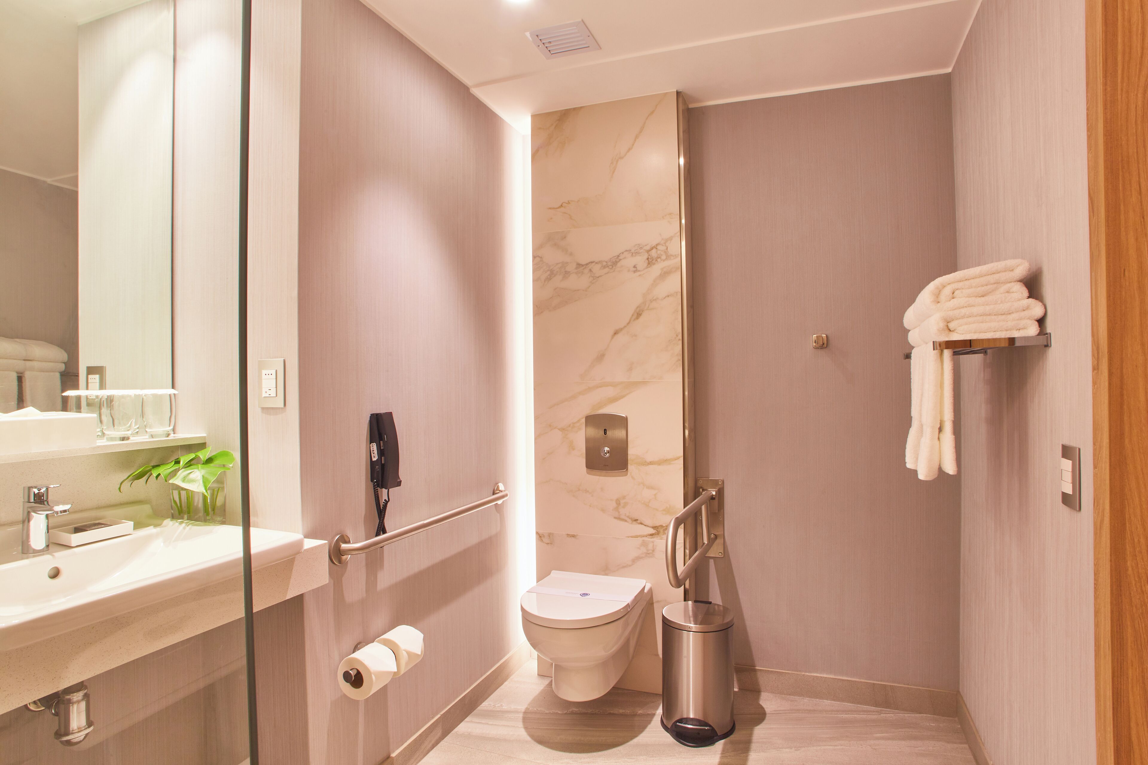 Une salle de bain moderne avec un mur en marbre, des toilettes, un lavabo avec un verre d’eau et un porte-serviettes.