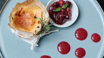 A plate with a pastry, a small bowl of red sauce, and a sprig of rosemary.
