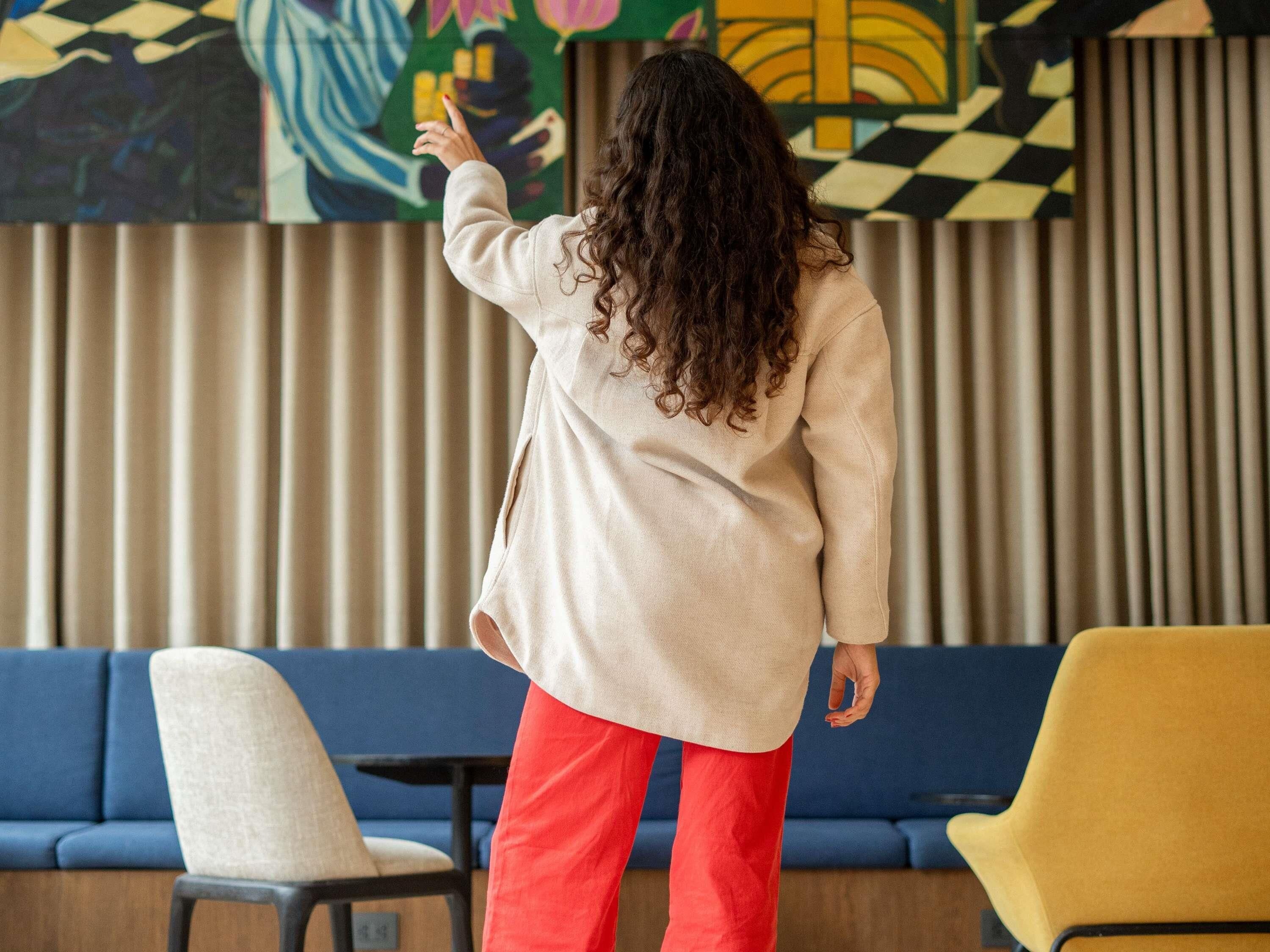 A person standing in a room with a blue sofa, a yellow chair, and a patterned wall.