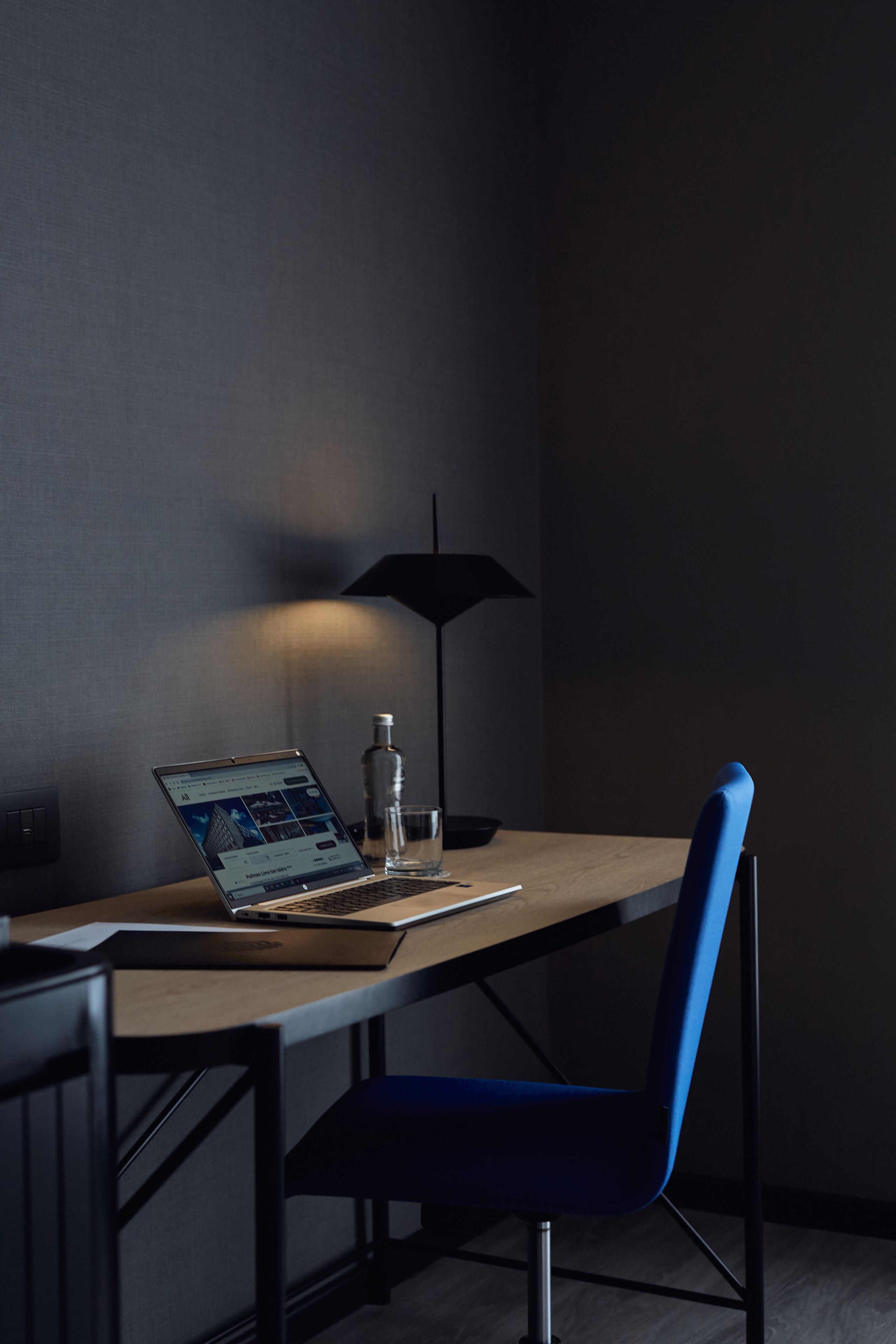 A modern office chair, a laptop on a desk, a glass of water, and a black floor lamp.