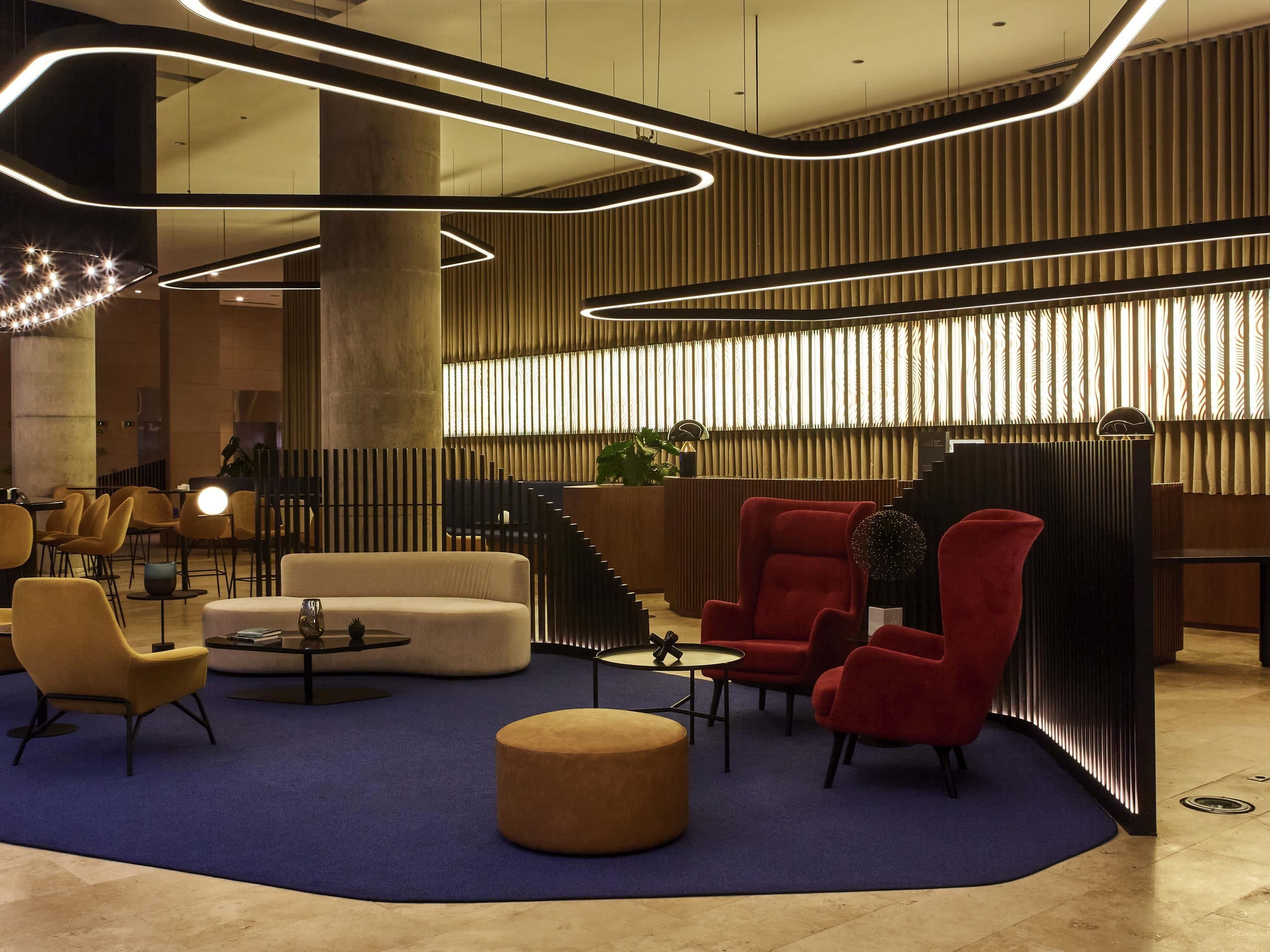 A modern lobby with a blue carpet, a reception desk, and red armchairs.