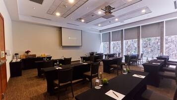 A conference room with multiple tables and chairs, a projector screen, and a large window with a city view.