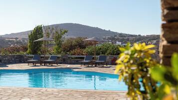 A swimming pool with lounge chairs and umbrellas, surrounded by greenery and a view of a hill.