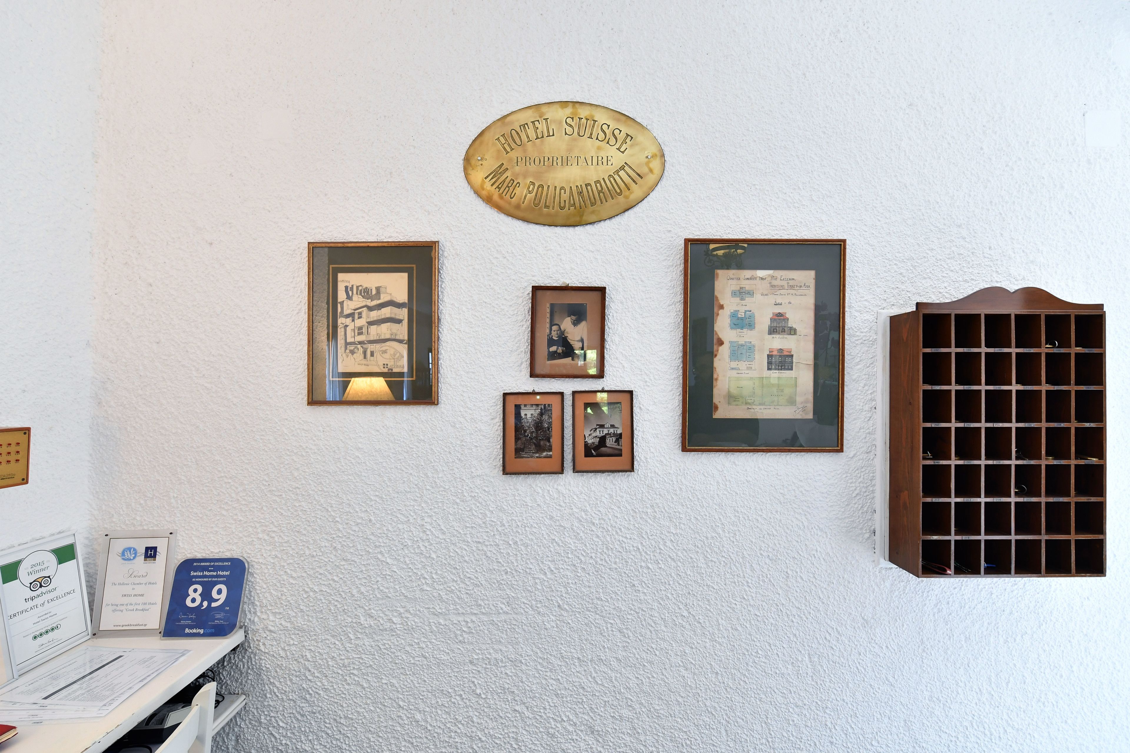 Un mur orné d’une plaque portant l’inscription « Hôtel Suisse, propriétaire : Marco Policarriotti », de tableaux encadrés et d’une fenêtre à carreaux.