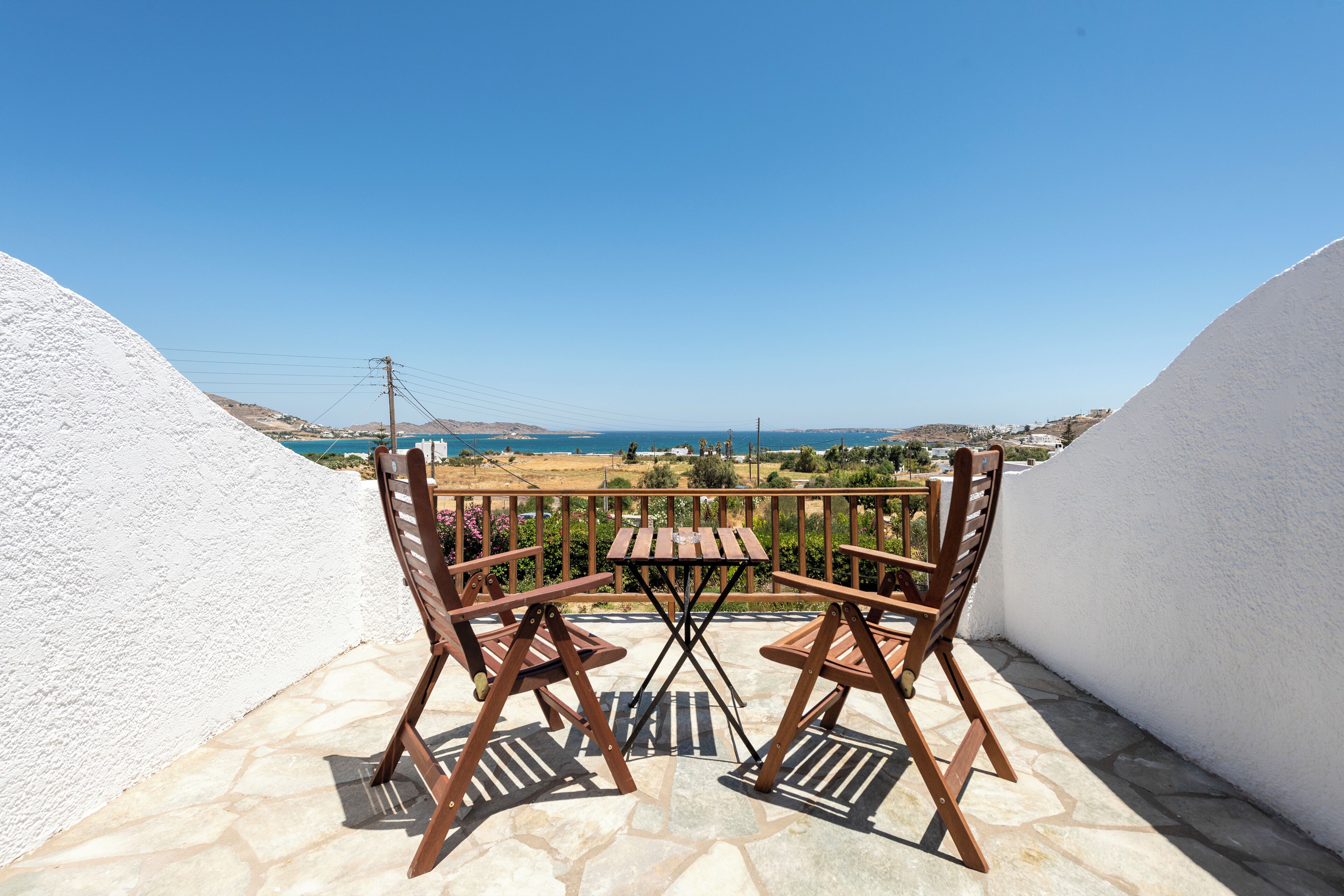 Eine Terrasse mit zwei Holzstühlen und einem Tisch, mit Blick auf eine Küstenlandschaft.