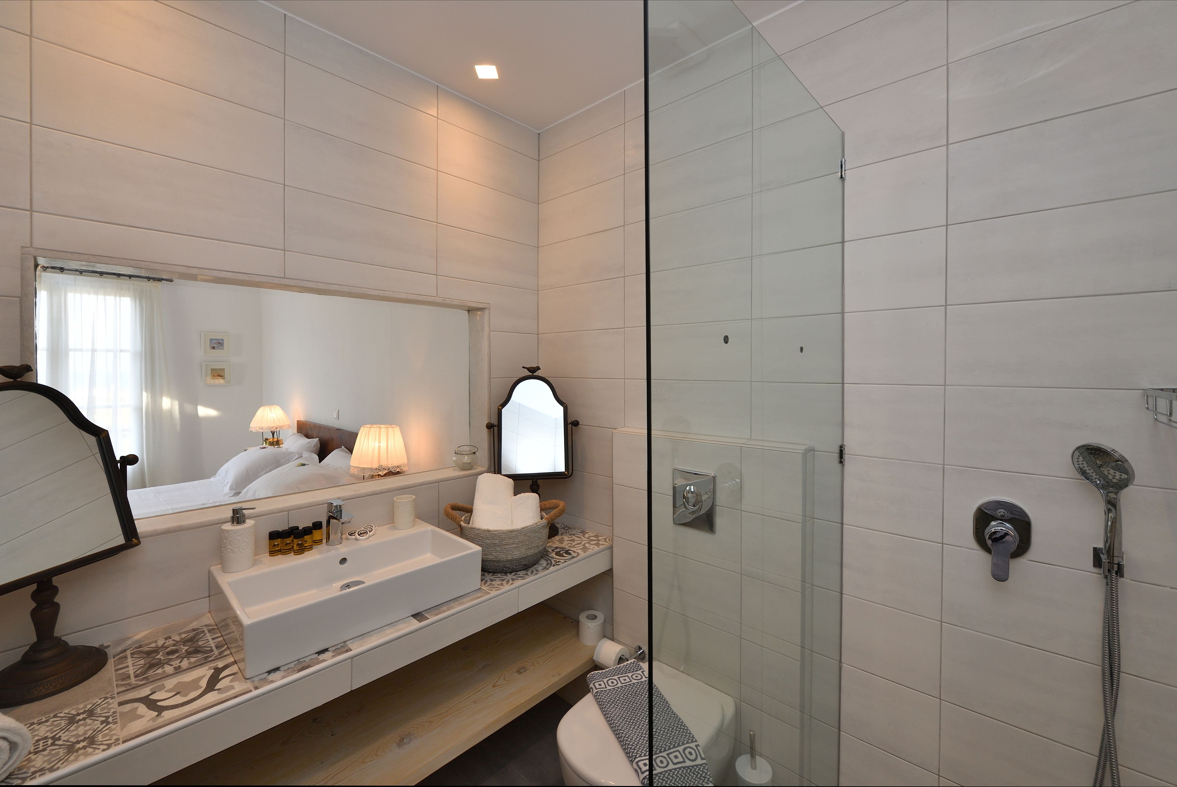 Une salle de bain moderne avec un grand miroir, un lavabo avec des articles de toilette, une douche équipée d’un pommeau de douche à main et des toilettes.