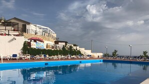 A swimming pool with lounge chairs and a building with a mural in the background. - Costa Makauda Residence (Sciacca)
