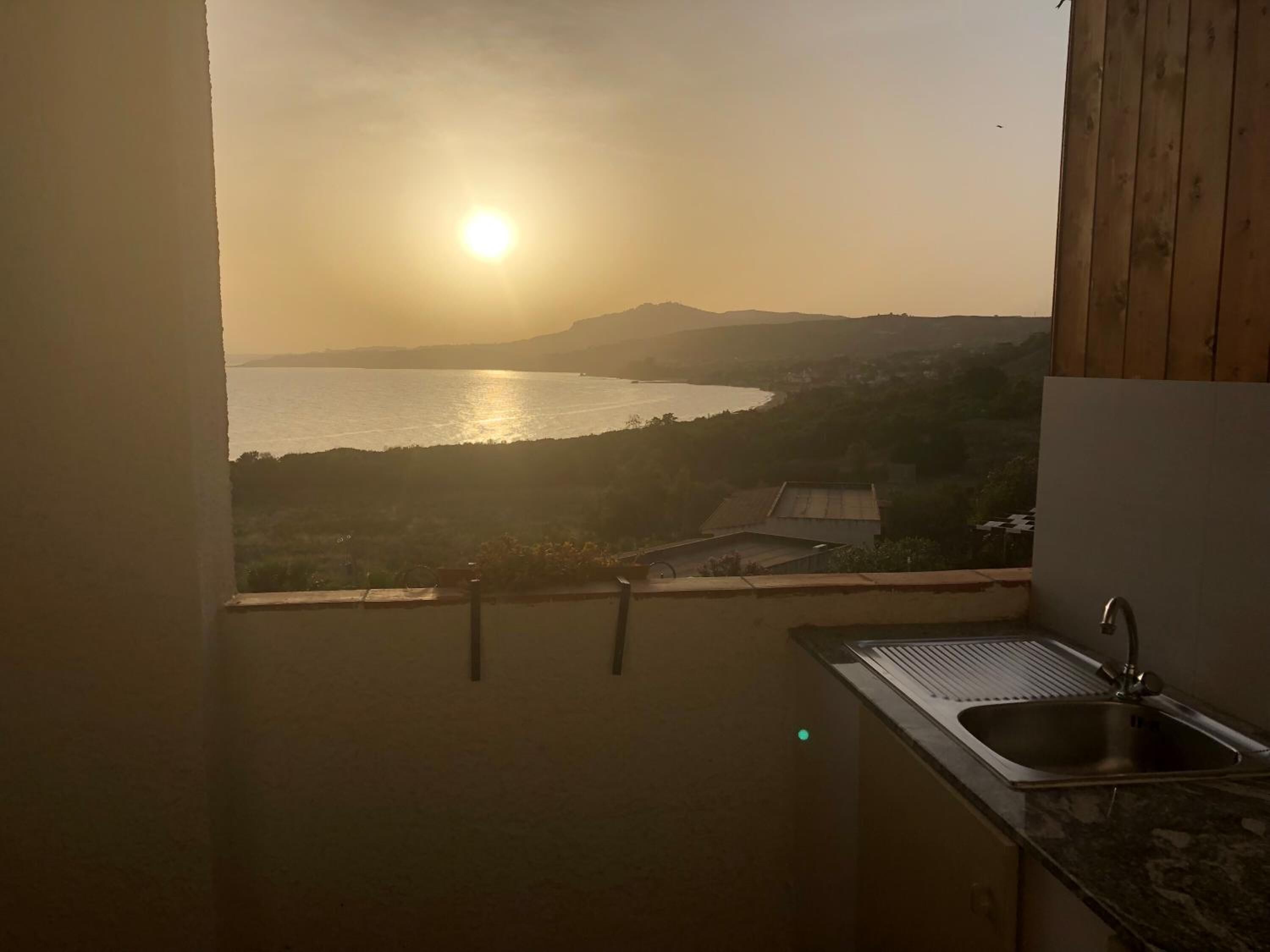 Una cocina con un lavabo y vistas a un cuerpo de agua y colinas durante el atardecer.