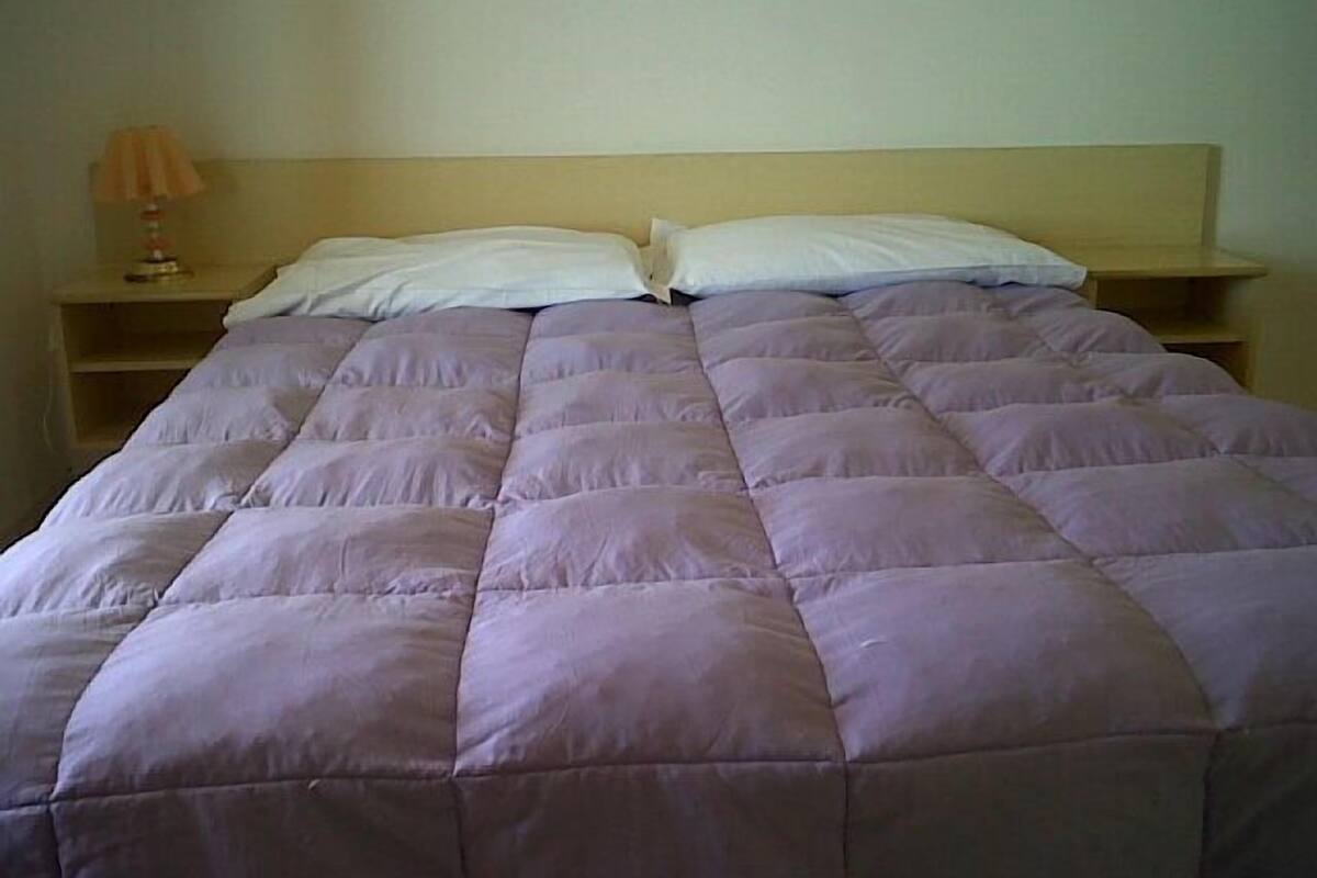 A bed with a light-colored headboard and a simple bedside table with a lamp.