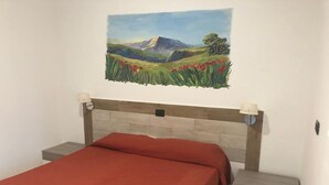 A bedroom with a bed, nightstands, a headboard, and a painting of a landscape. - Costa Makauda Residence (Sciacca)
