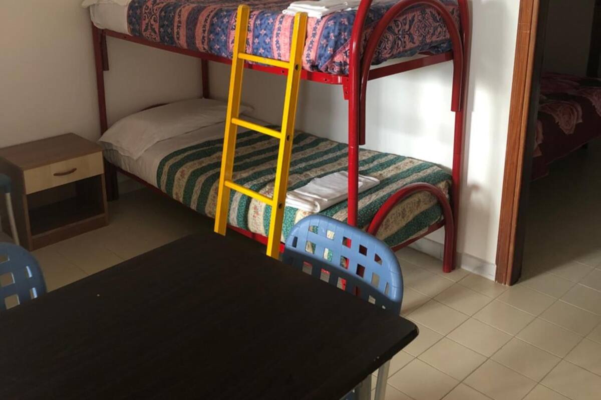 A bunk bed with a ladder, a small table, and a chair in a room with tiled flooring.