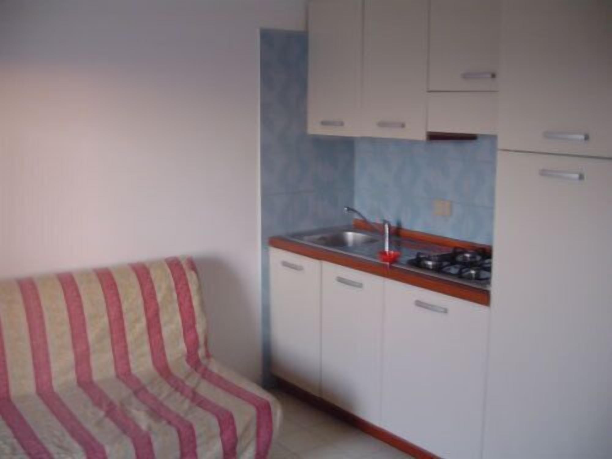 A small kitchenette with a stove, sink, and cabinets.