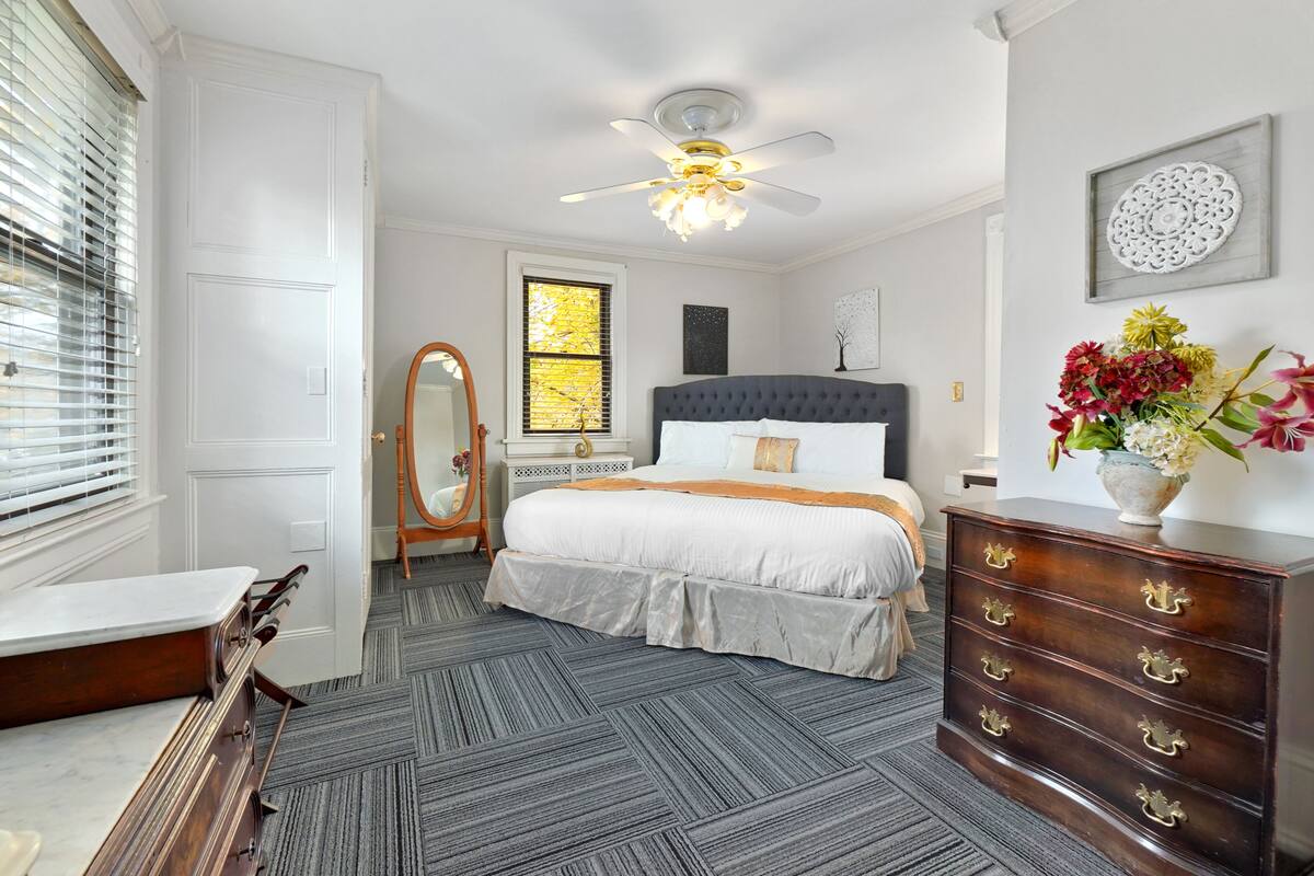 A bedroom with a bed, dresser, vanity, and a ceiling fan.
