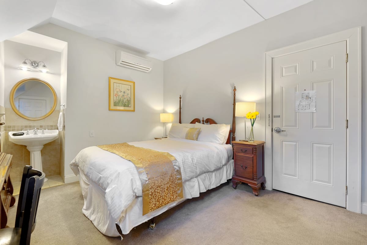 A bedroom with a bed, bedside table, lamp, and a door with a notice on it.