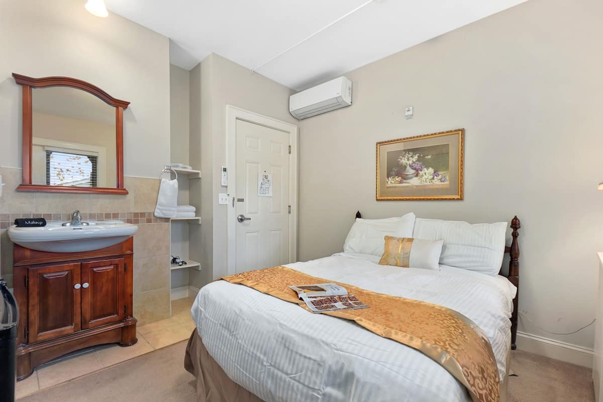 A bedroom with a bed, a wooden dresser, a sink, and a mirror.
