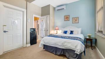 A bedroom with a large bed, a bedside table, an air conditioning unit, and a door with a whiteboard.