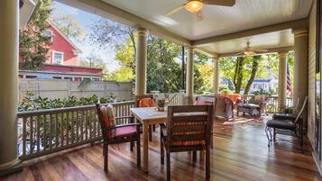 A covered porch with wooden flooring, a table, chairs, and a ceiling fan.