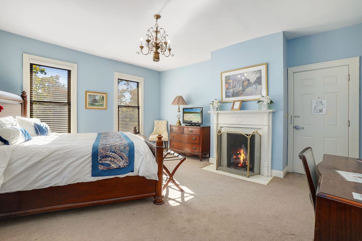 A bedroom with a bed, a fireplace, a television, and a desk.