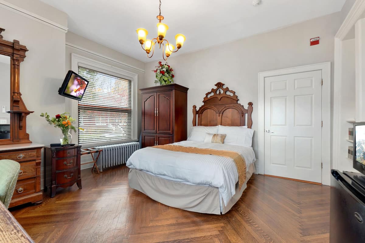 A bedroom with a bed, dresser, TV, and a chandelier.