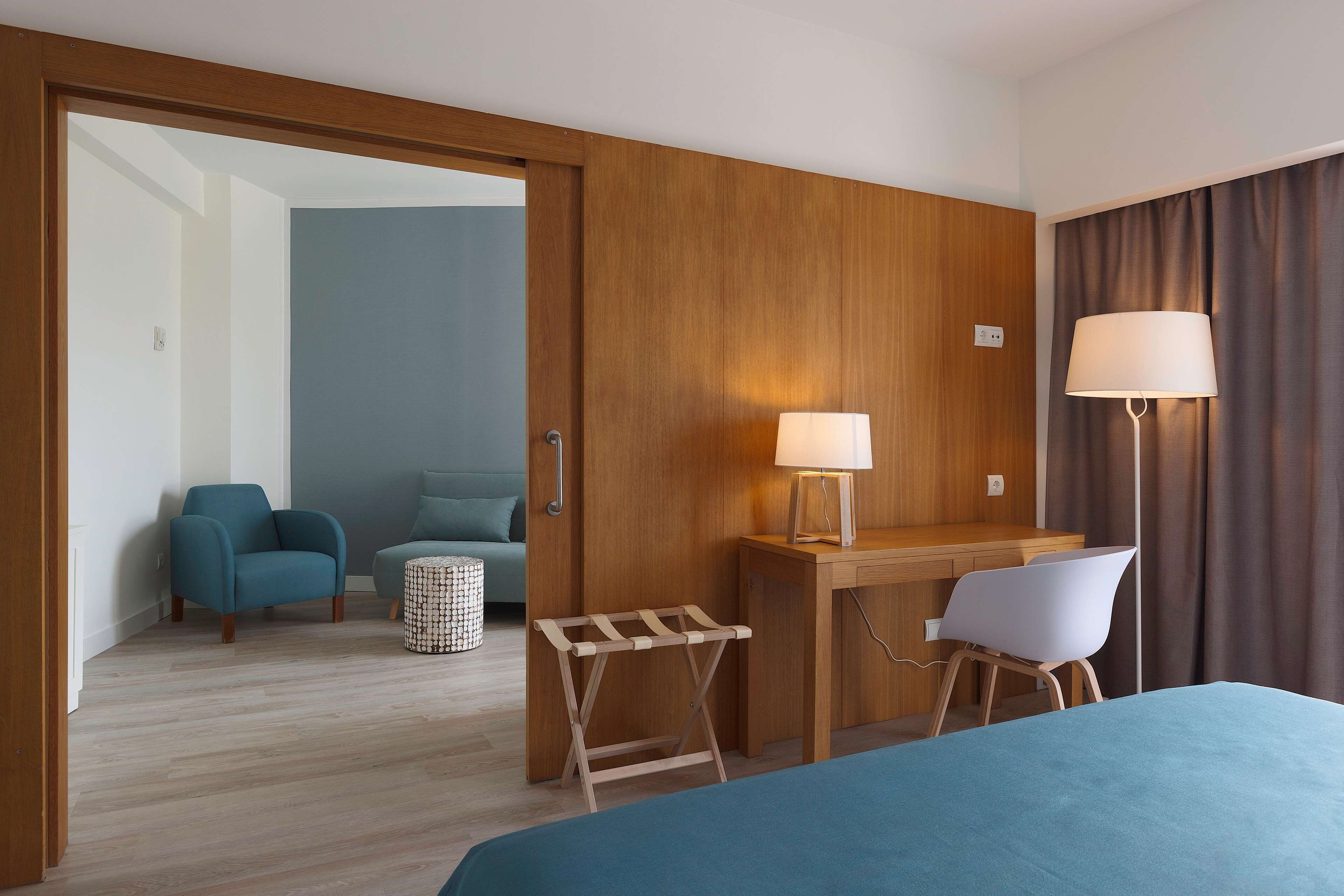 Una habitación de hotel con cama, escritorio con lámpara, silla y una pequeña mesa.