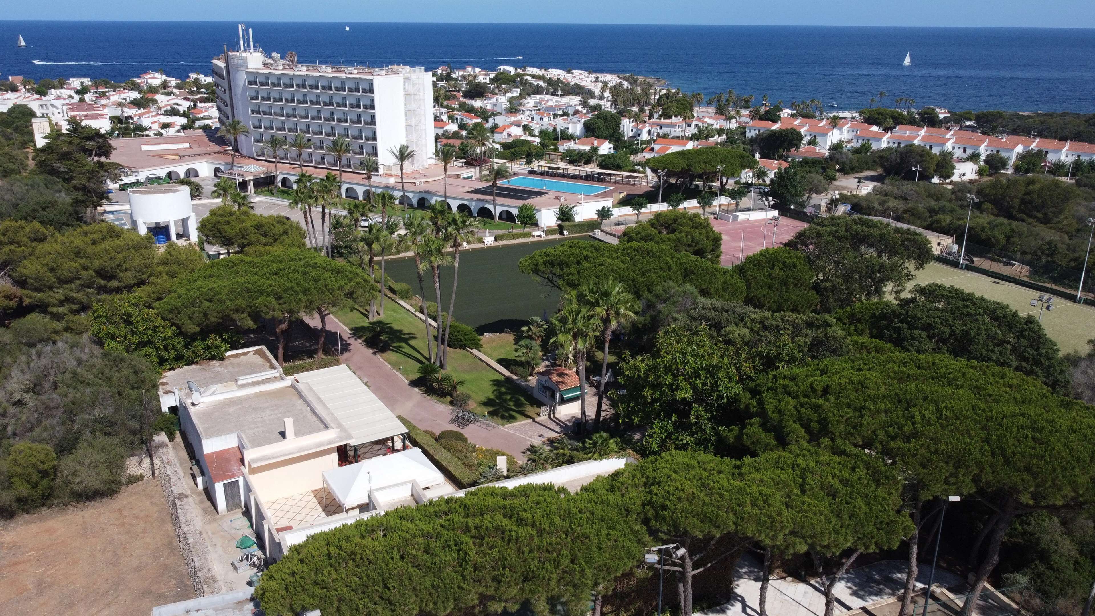 An aerial view of a coastal town with a large hotel, a swimming pool, and a marina.