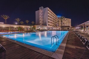 A swimming pool with a wooden deck, surrounded by lounge chairs and palm trees. - Alua Illa de Menorca Hotel (Sant Lluis)