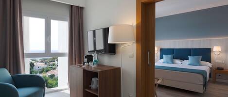 A hotel room with a bed, a desk with a flat-screen TV, a lamp, and a view of the city.