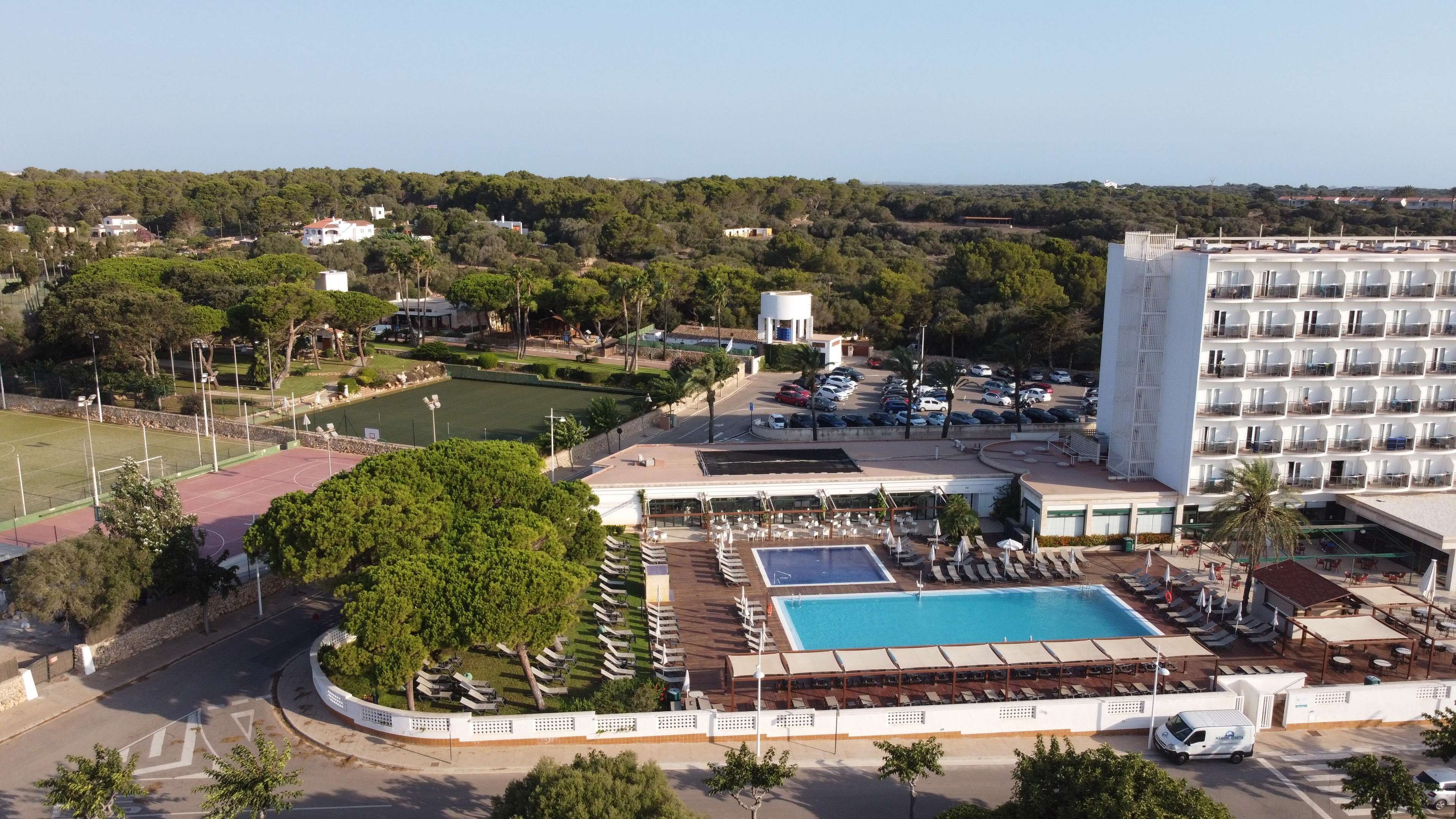 A hotel with a swimming pool, outdoor seating, and a tennis court.