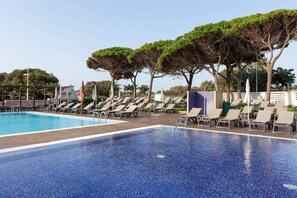 A pool with clear blue water, surrounded by lounge chairs and trees. - Alua Illa de Menorca Hotel (Sant Lluis)