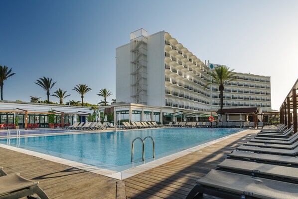 A swimming pool with sun loungers and a building with balconies in the background. - Alua Illa de Menorca Hotel (Sant Lluis)