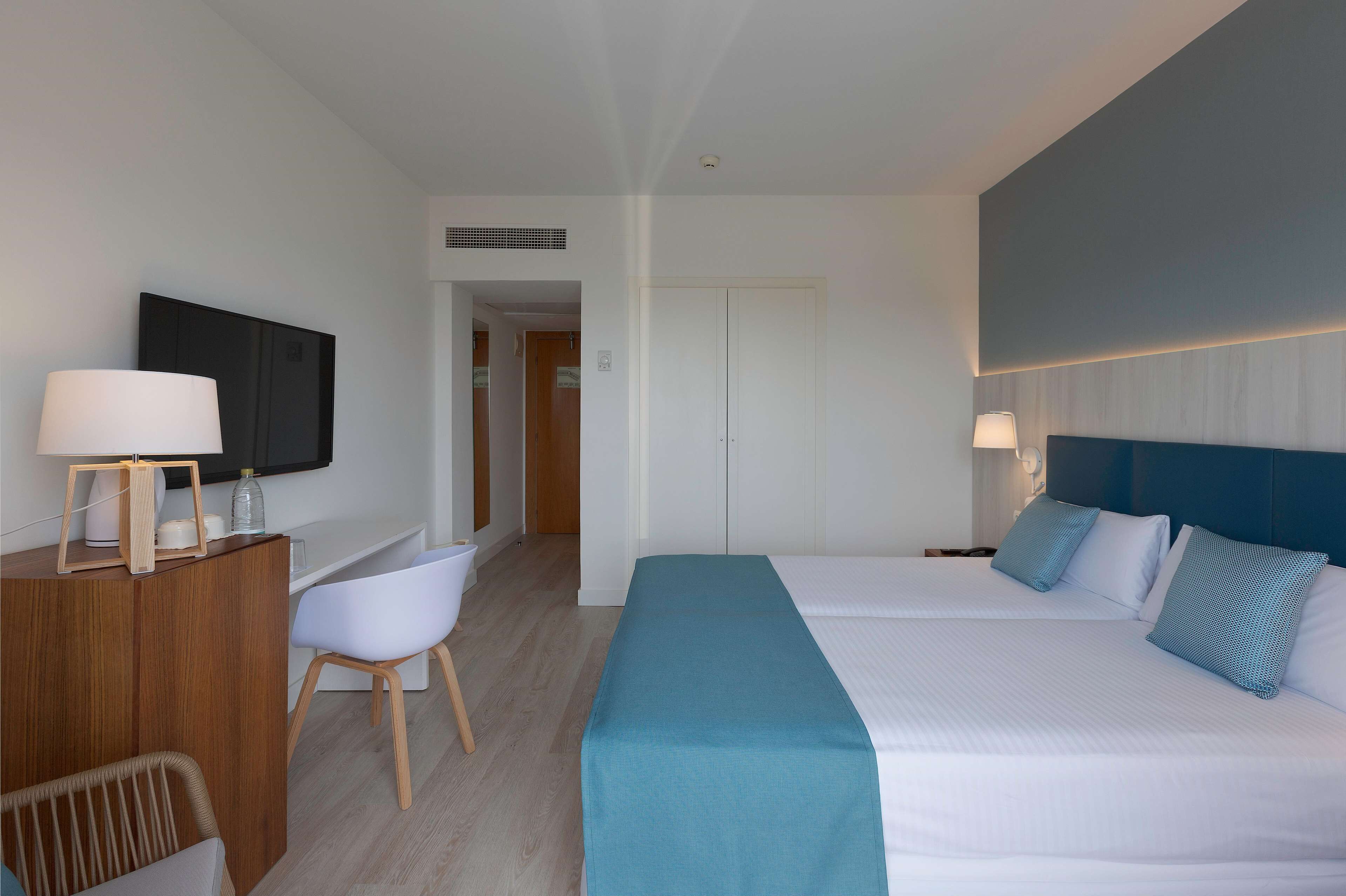 Una habitación de hotel con cama, escritorio, silla y televisor en la pared.