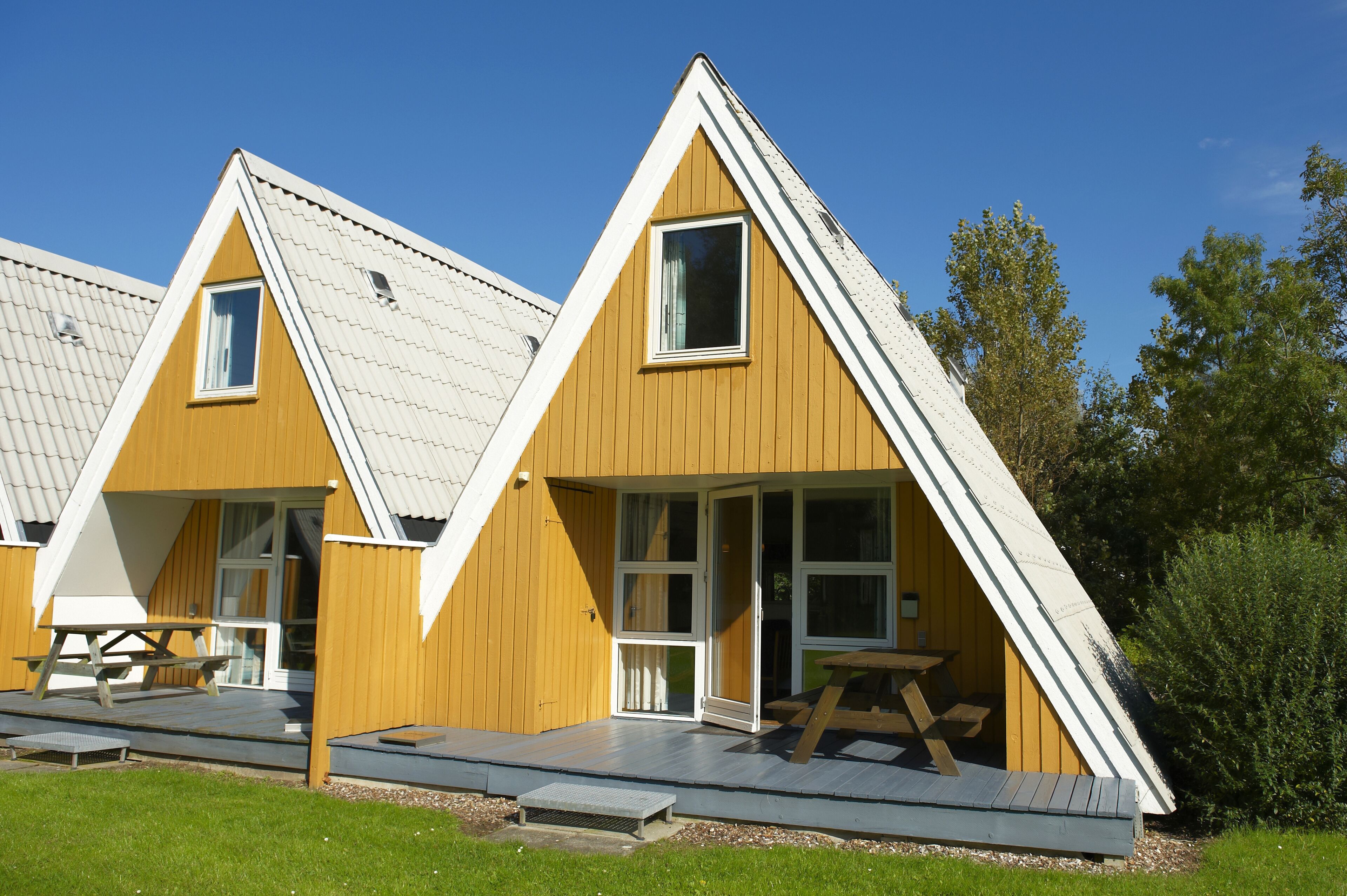 A row of triangular-roofed cabins with sliding glass doors and a picnic table in front.