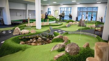 Un campo de mini golf con un hoyo de cocodrilo, rocas e una bandera sobre césped artificial.