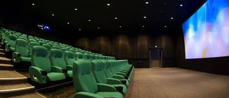 A theater with rows of green seats, a large screen, and a dark interior.