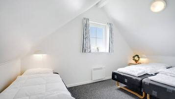 Une petite pièce bien éclairée, avec deux lits, une fenêtre avec des rideaux, un radiateur et un luminaire fixé au mur.