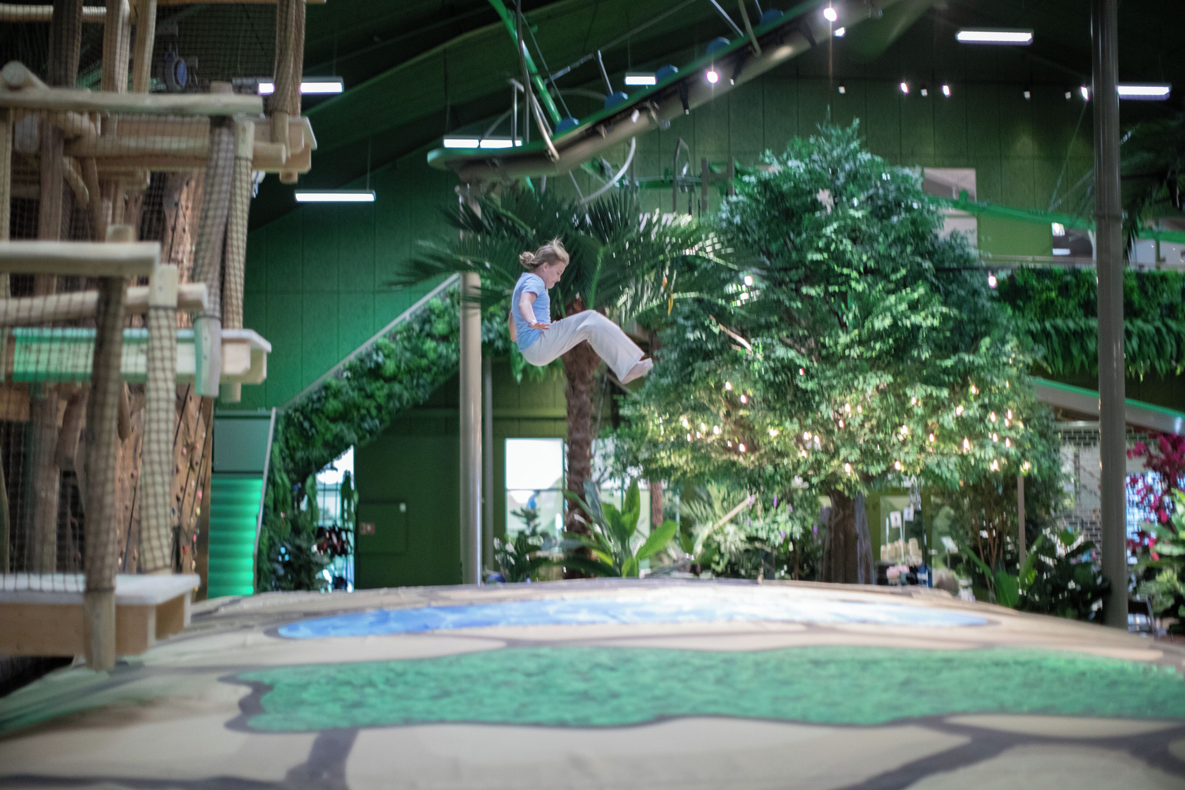 Un espace de jeux intérieur comprenant une structure d’escalade, un grand arbre et une surface de jeu souple.