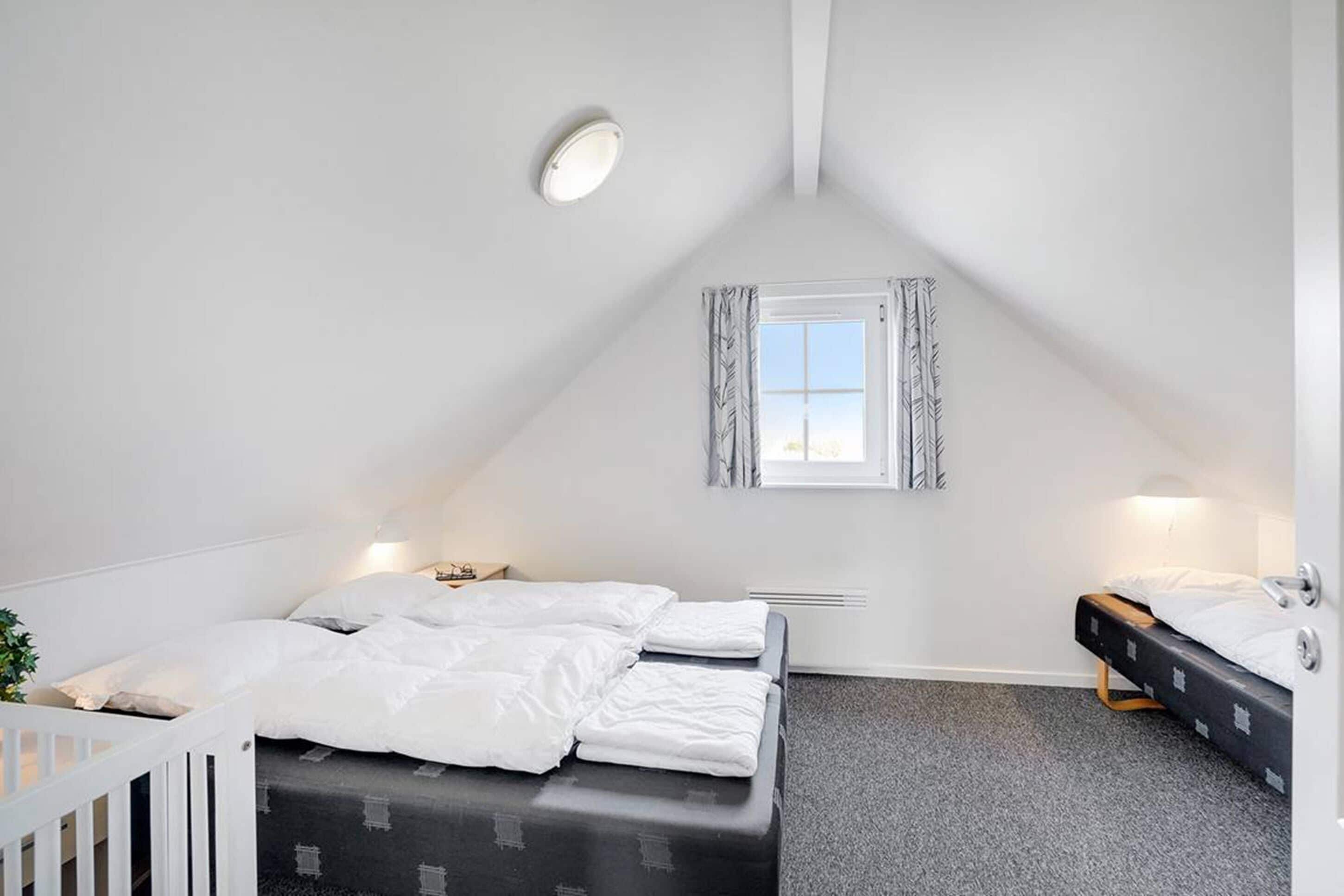 Um quarto pequeno e bem iluminado com uma cama de solteiro, um berço e uma janela com cortinas.