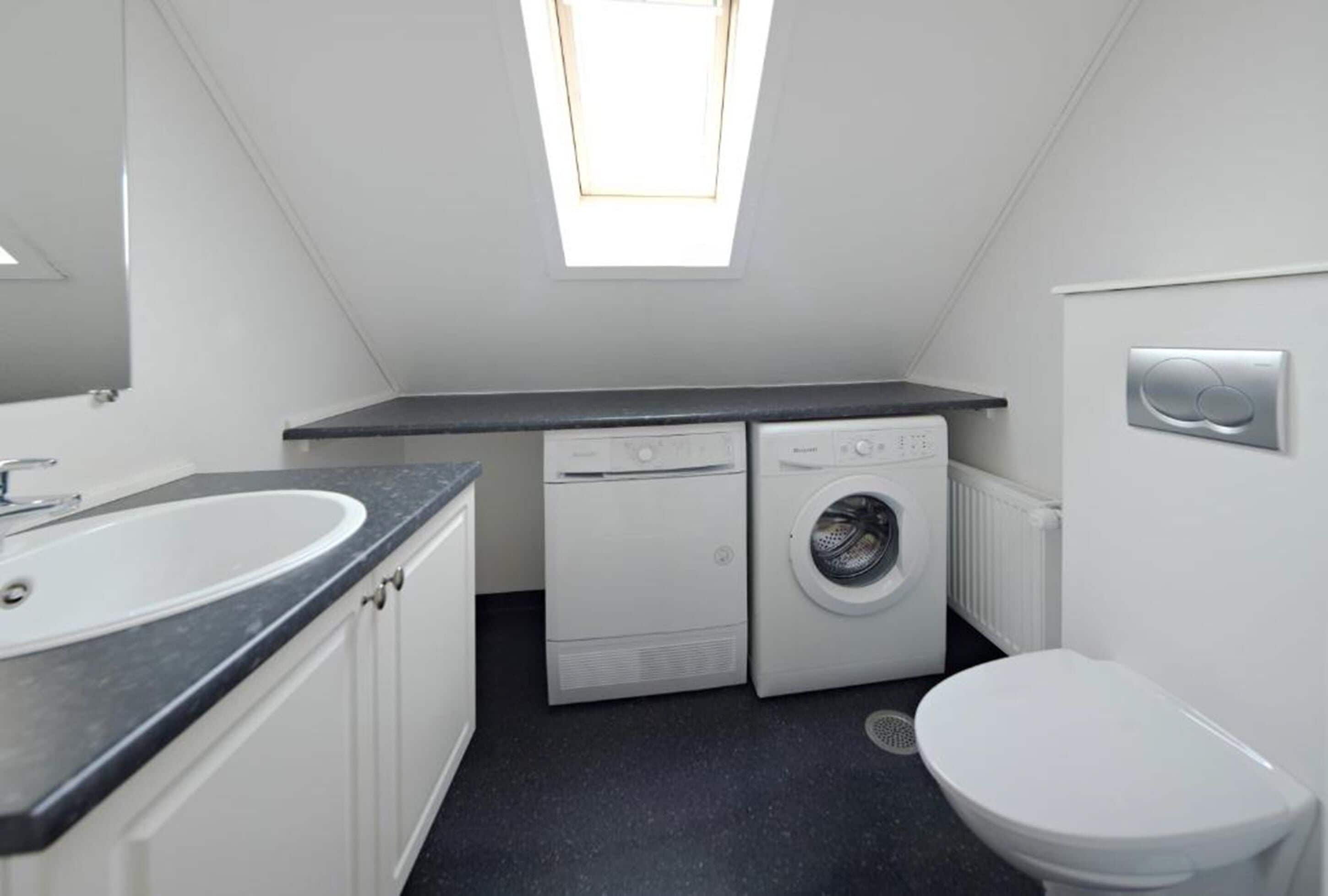Une salle de bain moderne et compacte, dotée d’un puits de lumière, d’un lave-linge, de toilettes et d’un lavabo.