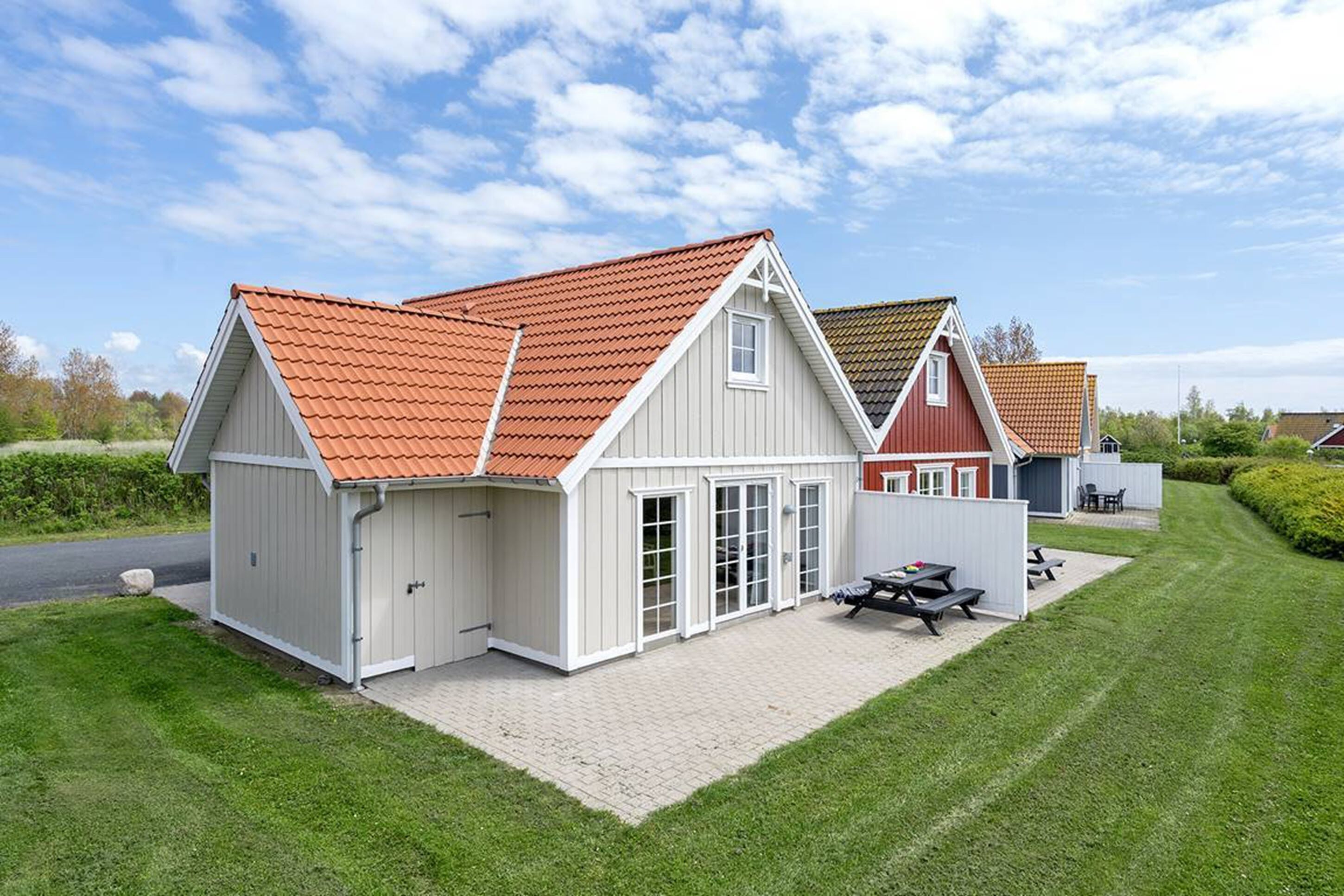 A two-story house with a red-tiled roof, a covered patio with a table and chairs, and a small shed.