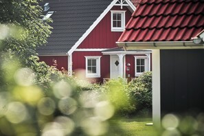 A red house with a white door and windows, surrounded by greenery.