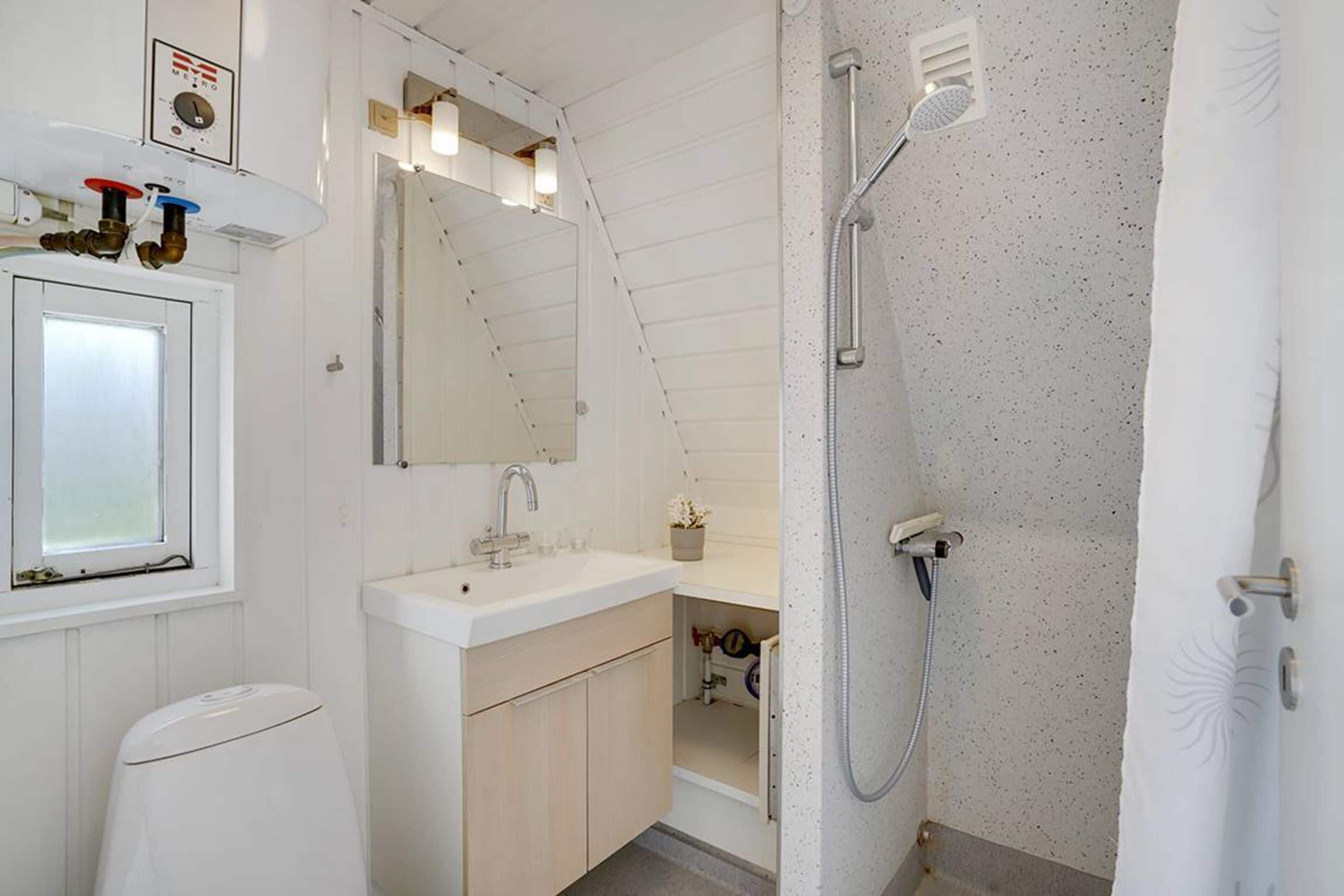 Et badeværelse med hvid vask, spejl og brusebad.