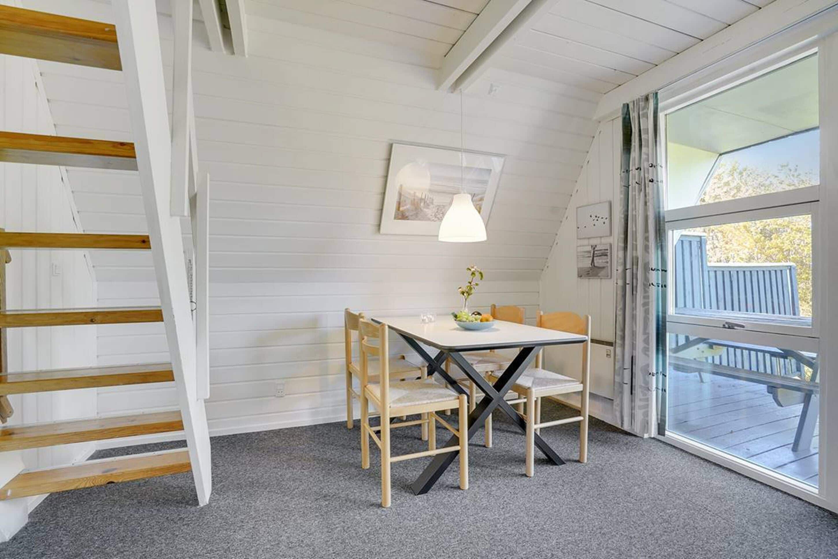 A cozy room with a wooden table and chairs, a framed picture on the wall, and a large window with a view of the outdoors.
