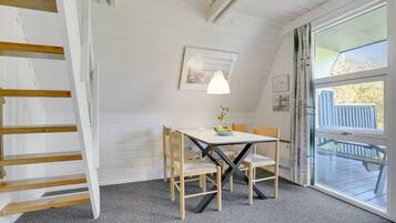 A cozy room with a wooden table and chairs, a framed picture on the wall, and a large window with a view of the outdoors.